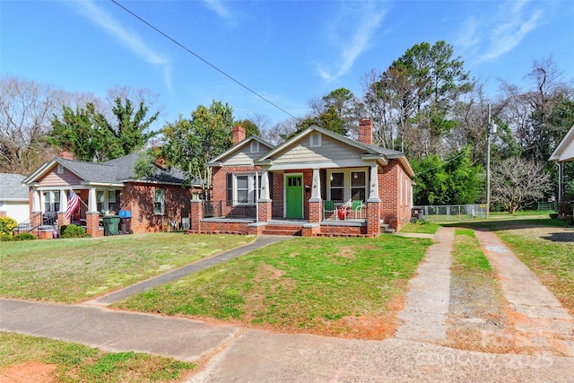 view of front facade with brick siding, a chimney, covered porch, a front yard, and driveway