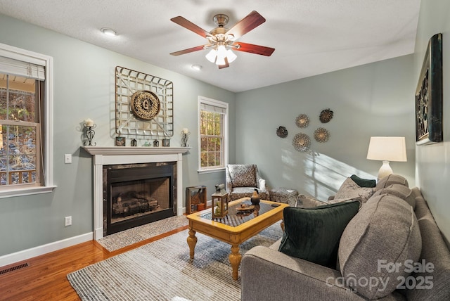 living room with baseboards, visible vents, a ceiling fan, a premium fireplace, and wood finished floors