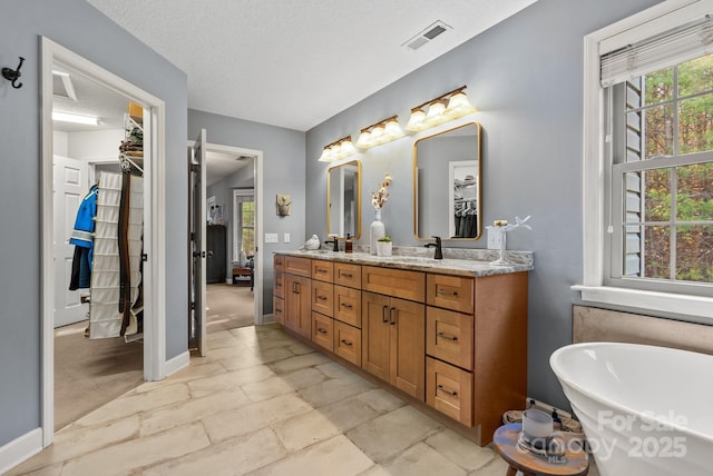 full bath with double vanity, visible vents, a spacious closet, a freestanding tub, and a sink