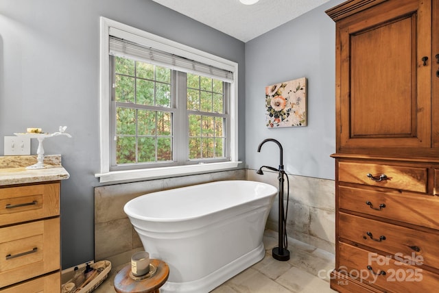 full bathroom with a textured ceiling, a soaking tub, vanity, and tile walls