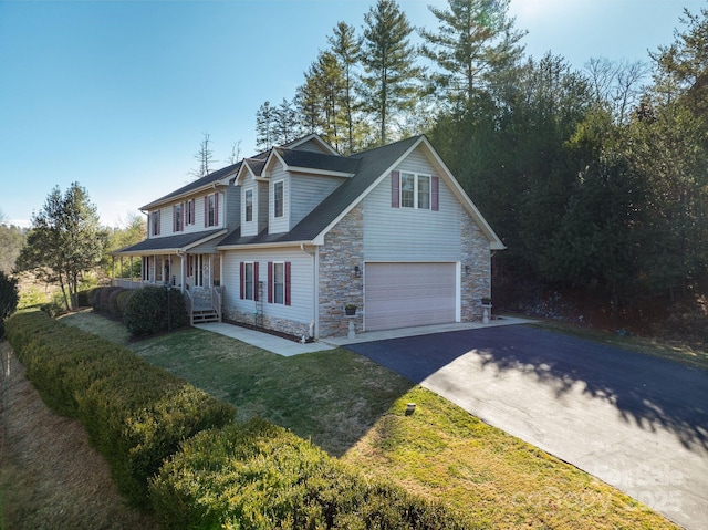 view of front of house featuring a garage, covered porch, stone siding, driveway, and a front lawn