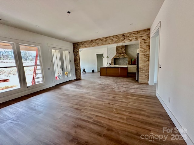 unfurnished living room with brick wall, wood finished floors, and baseboards