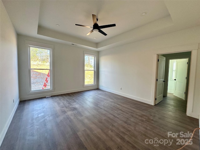 empty room with a raised ceiling, dark wood finished floors, and baseboards