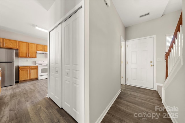 hallway featuring dark wood-type flooring, visible vents, baseboards, and stairs