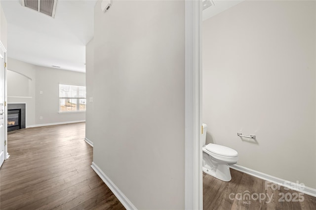 bathroom featuring toilet, visible vents, wood finished floors, and a glass covered fireplace