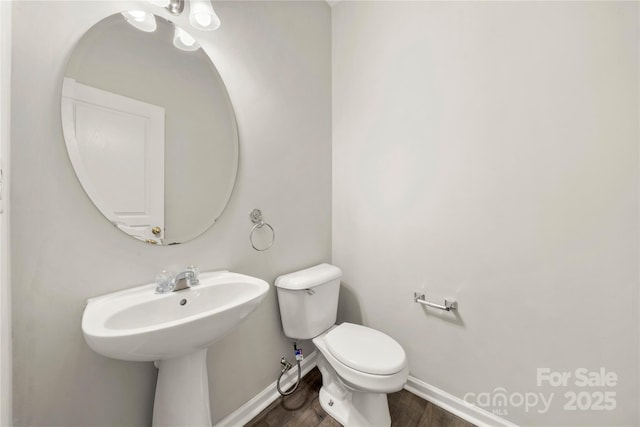 half bathroom with wood finished floors, toilet, and baseboards