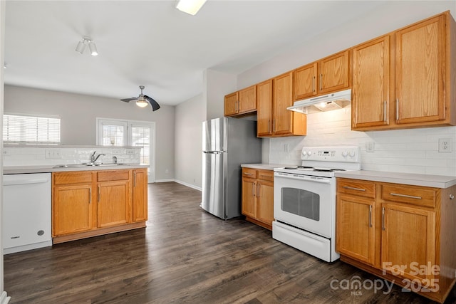 kitchen featuring under cabinet range hood, white appliances, dark wood-style flooring, a sink, and light countertops