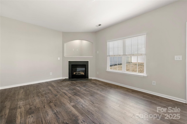 unfurnished living room featuring a glass covered fireplace, visible vents, dark wood finished floors, and baseboards