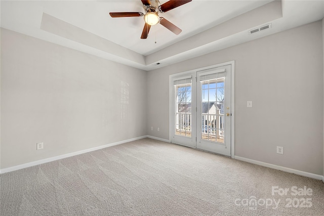 carpeted empty room with a ceiling fan, a raised ceiling, visible vents, and baseboards