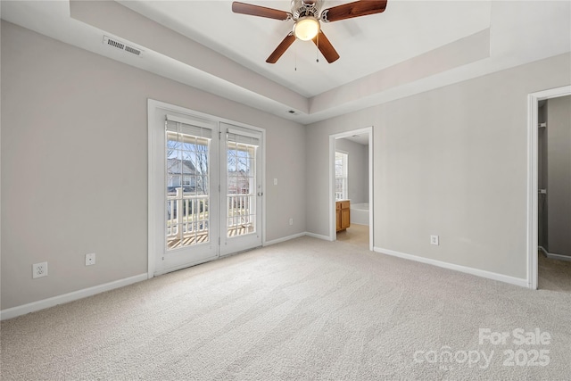 unfurnished room featuring ceiling fan, light carpet, visible vents, baseboards, and a tray ceiling