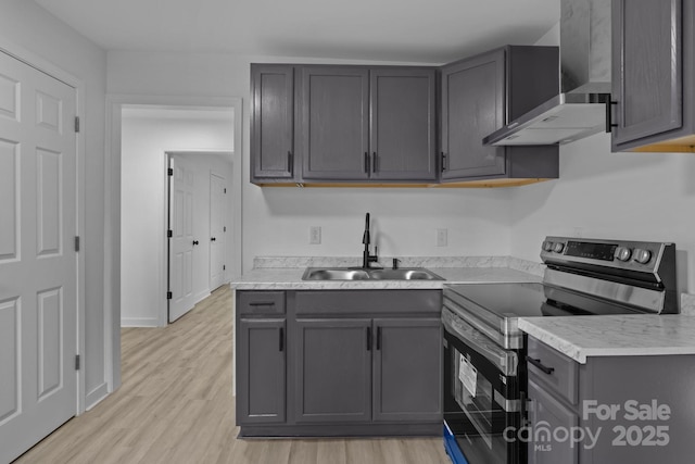 kitchen featuring a sink, wall chimney range hood, light wood finished floors, and electric stove