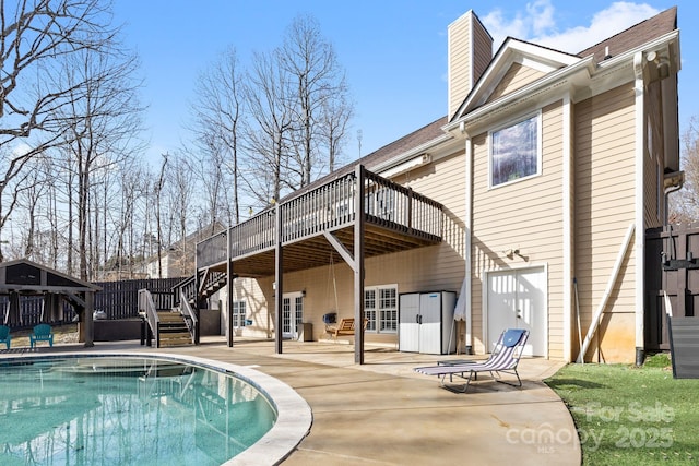 back of property featuring a chimney, a patio area, a deck, an outdoor pool, and stairs