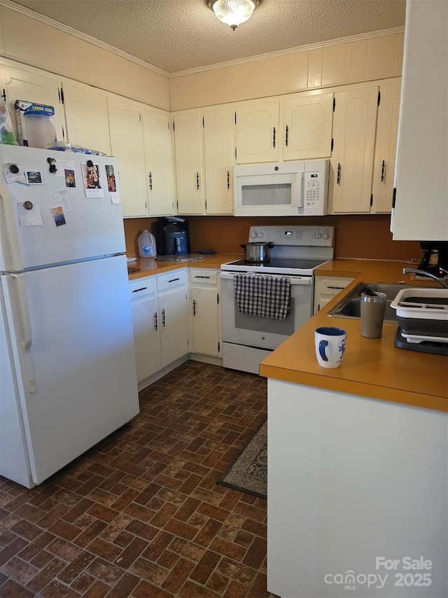 kitchen featuring brick floor, ornamental molding, white cabinetry, a sink, and white appliances