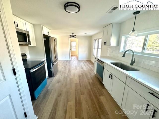 kitchen with a sink, stainless steel appliances, light countertops, and white cabinetry