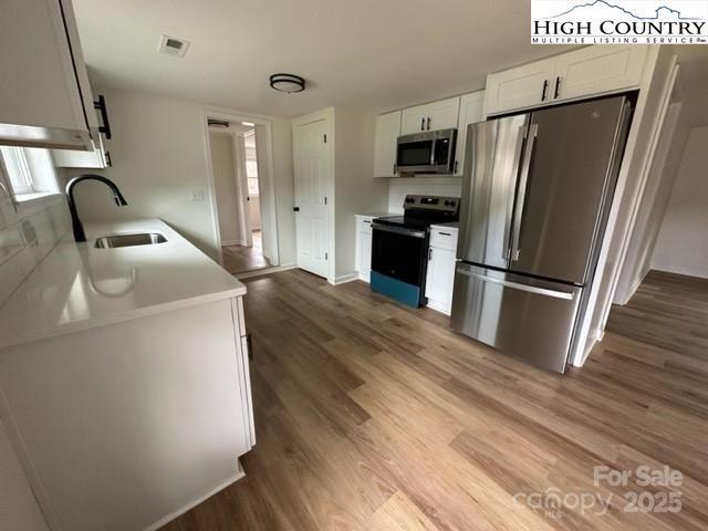 kitchen with visible vents, white cabinets, stainless steel appliances, light countertops, and a sink