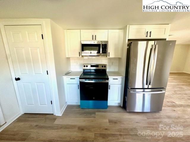 kitchen featuring light wood-style floors, white cabinets, light countertops, appliances with stainless steel finishes, and backsplash