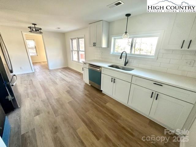 kitchen featuring visible vents, white cabinets, dishwasher, light countertops, and a sink