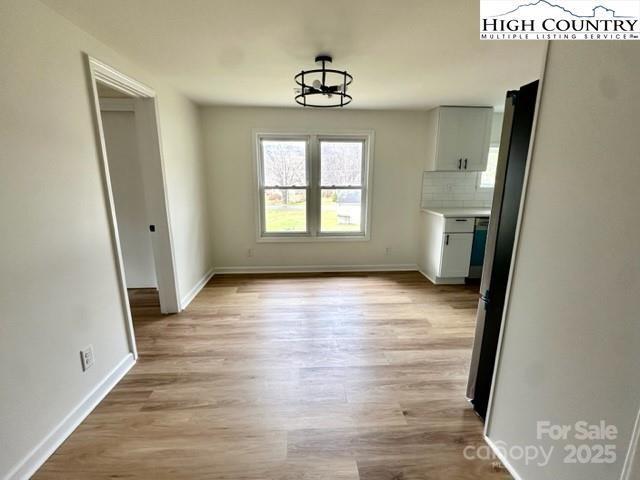 unfurnished dining area featuring baseboards, a notable chandelier, and light wood finished floors