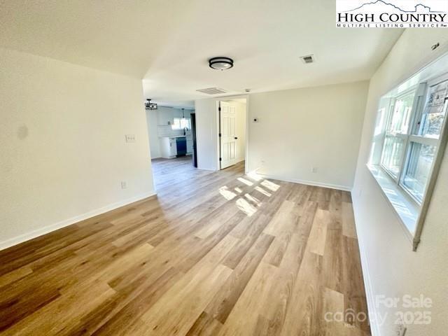 spare room with light wood-type flooring, visible vents, and baseboards