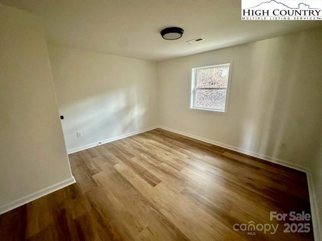 spare room with baseboards, visible vents, and wood finished floors