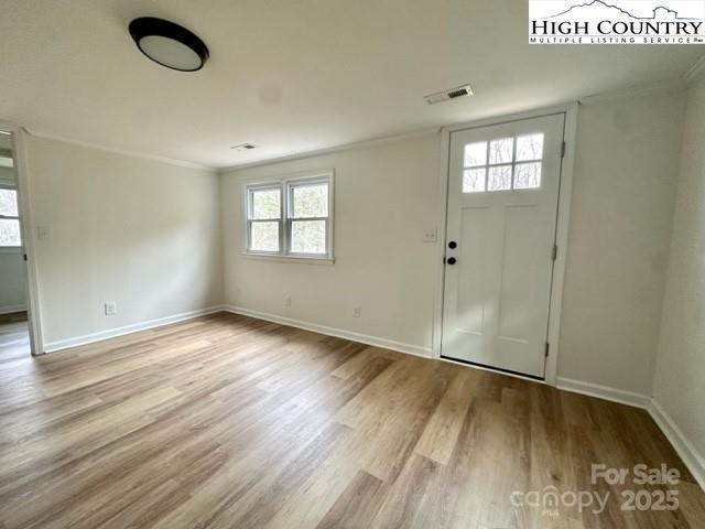 entryway with crown molding, baseboards, visible vents, and light wood-style floors