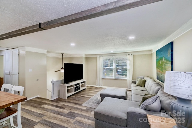 living room with a textured ceiling, wood finished floors, baseboards, ornamental molding, and beam ceiling