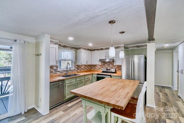 kitchen featuring butcher block countertops, a sink, appliances with stainless steel finishes, decorative backsplash, and light wood finished floors