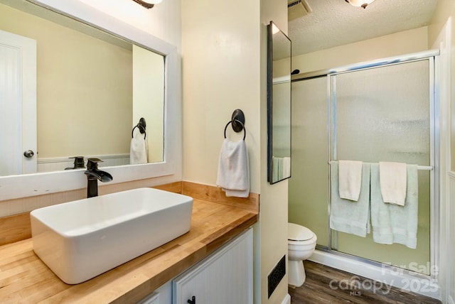 bathroom featuring a textured ceiling, toilet, wood finished floors, vanity, and a stall shower