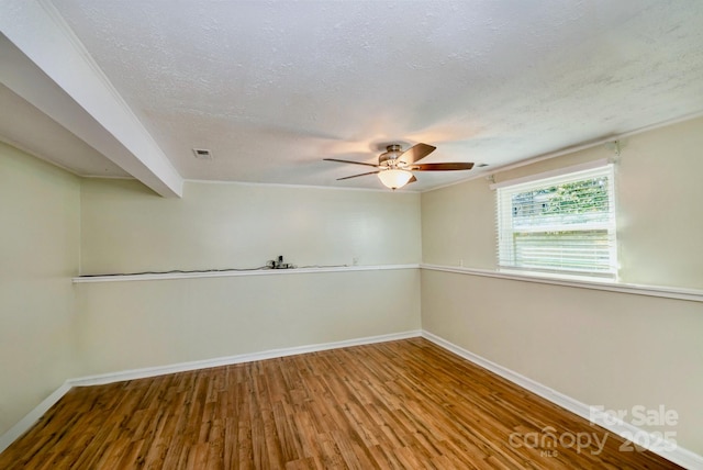 spare room featuring a textured ceiling, wood finished floors, visible vents, and baseboards