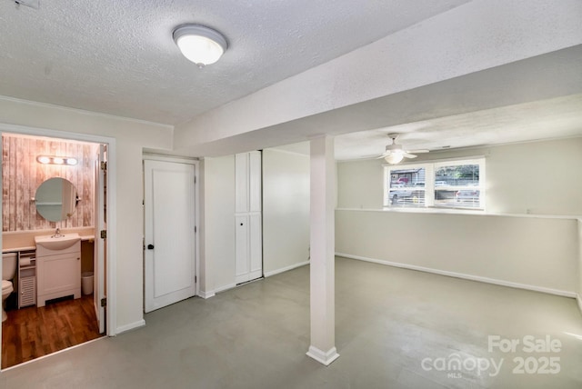 basement featuring a textured ceiling, ceiling fan, a sink, and baseboards