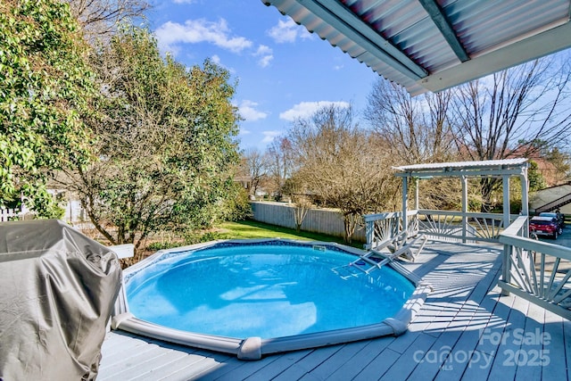 pool with a deck, grilling area, a fenced backyard, and a pergola