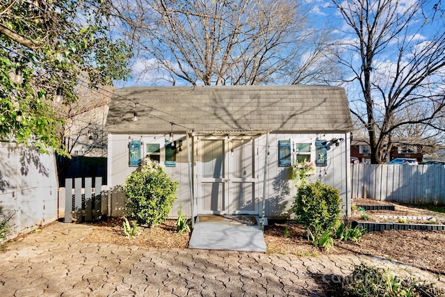 exterior space featuring a shingled roof, fence, mansard roof, and an outdoor structure