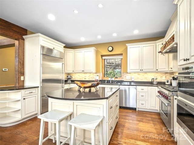 kitchen with a breakfast bar, a kitchen island, high quality appliances, open shelves, and dark countertops