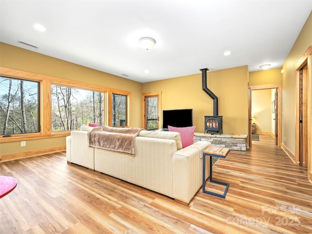 living area with recessed lighting, visible vents, baseboards, light wood finished floors, and a wood stove