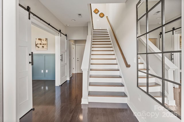 staircase with a barn door, visible vents, a decorative wall, and wood finished floors