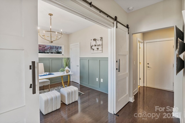 interior space featuring a barn door, a notable chandelier, a decorative wall, dark wood-style flooring, and wainscoting