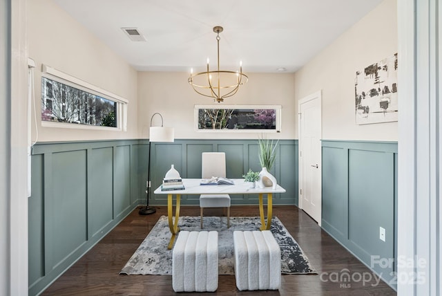 home office featuring dark wood finished floors, visible vents, a decorative wall, wainscoting, and a chandelier