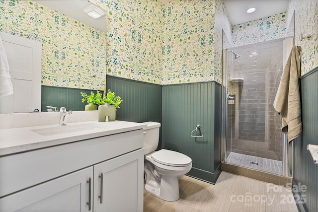 bathroom featuring toilet, wallpapered walls, a shower stall, and wainscoting