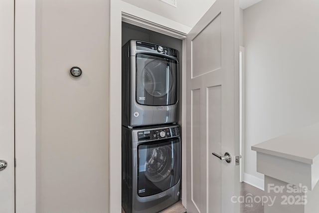 laundry area with laundry area, baseboards, and stacked washer / drying machine