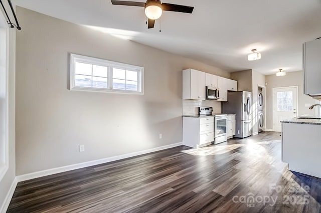 kitchen with stacked washer and clothes dryer, decorative backsplash, appliances with stainless steel finishes, white cabinetry, and a sink