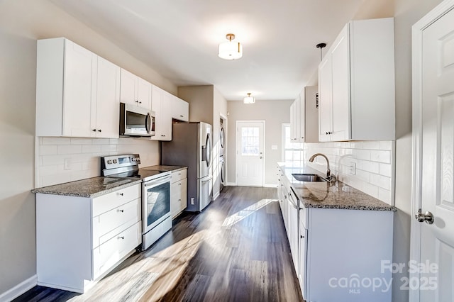 kitchen with stainless steel appliances, a sink, white cabinetry, dark stone counters, and pendant lighting