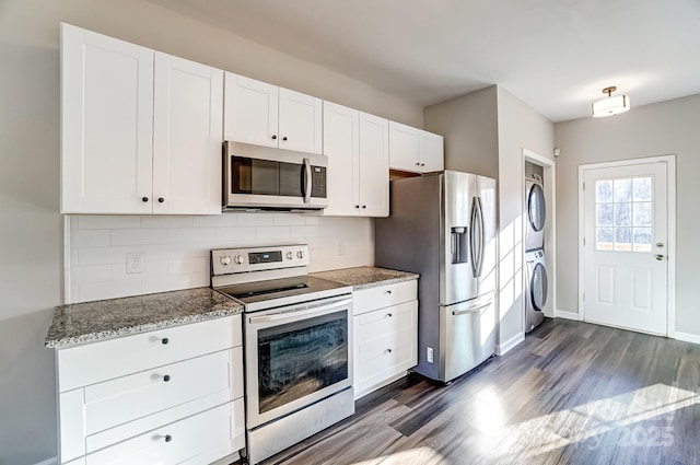 kitchen with stacked washing maching and dryer, white cabinetry, appliances with stainless steel finishes, and stone counters