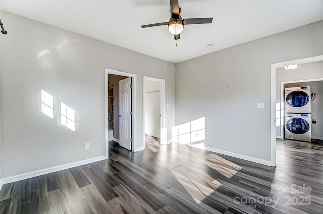 empty room featuring a ceiling fan, baseboards, dark wood-style flooring, and stacked washer and clothes dryer