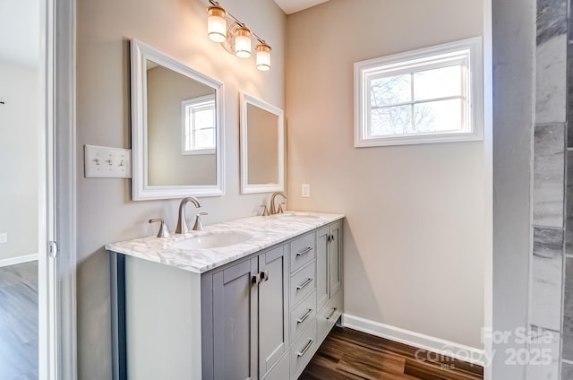 bathroom featuring wood finished floors, a sink, baseboards, and double vanity