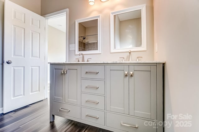 full bath featuring a sink, double vanity, and wood finished floors