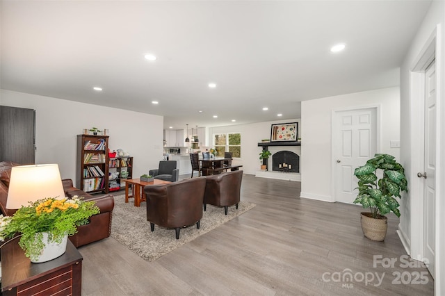 living area featuring recessed lighting, a fireplace with raised hearth, and light wood finished floors