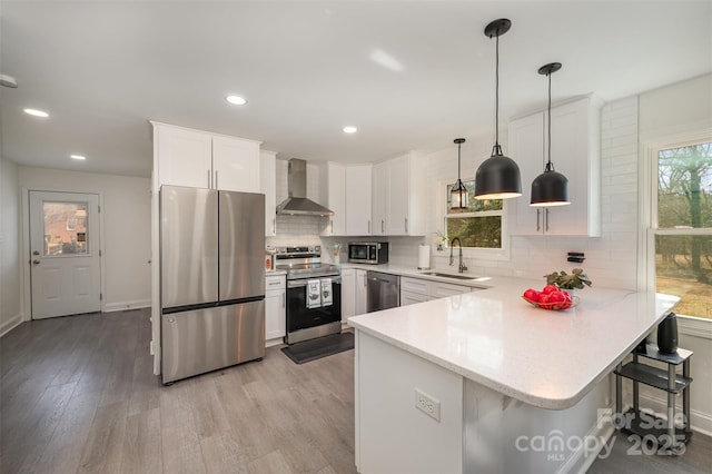 kitchen featuring wall chimney exhaust hood, appliances with stainless steel finishes, hanging light fixtures, light countertops, and white cabinetry