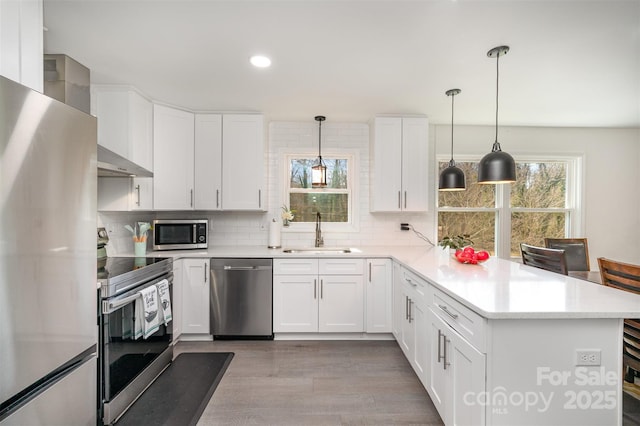 kitchen with stainless steel appliances, a sink, white cabinets, hanging light fixtures, and light countertops