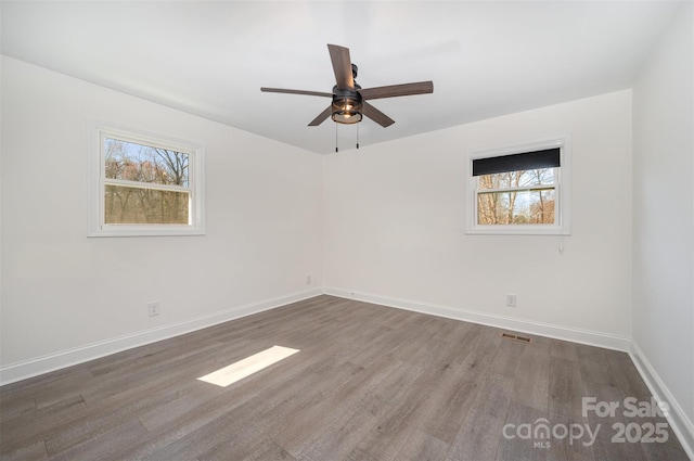 spare room with a ceiling fan, visible vents, baseboards, and wood finished floors