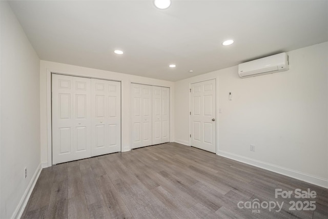 unfurnished bedroom featuring baseboards, a wall mounted air conditioner, light wood-style floors, multiple closets, and recessed lighting